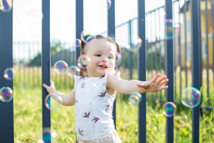 small child playing with bubbles near pool with aluminum fence